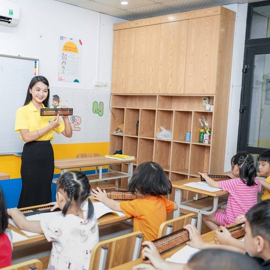 先生が教室の前でそろばんを持ち上げ、子どもたちが机の上のそろばんに向かっている