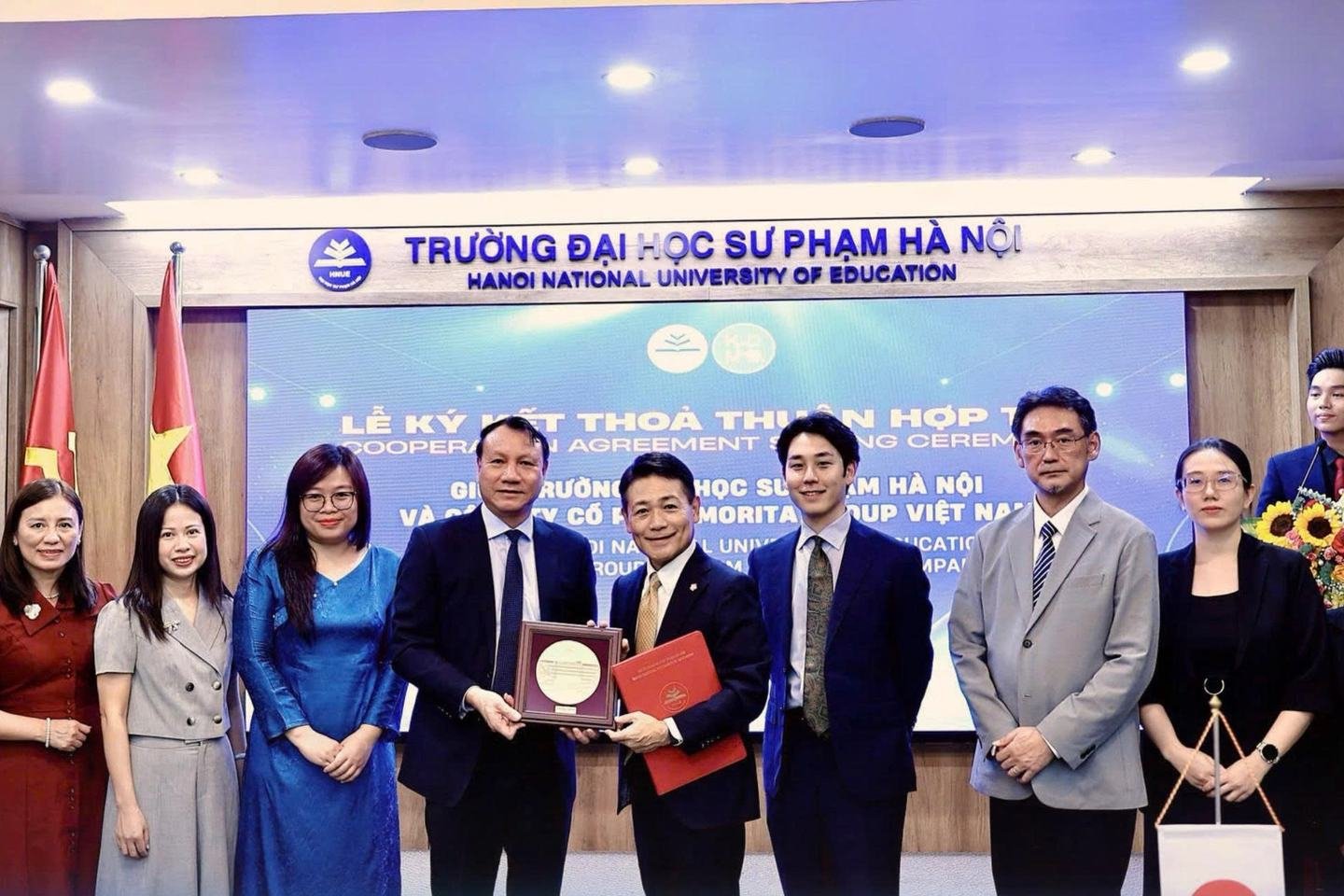Lãnh đạo hai bên cầm kỷ niệm chương và Biên bản ghi nhớ, cùng chụp ảnh với các đại biểu trước màn hình buổi lễ