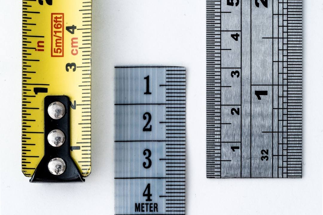 Một thước dây màu vàng có vạch cm và inch, một thước màu xanh nhạt in chữ METER và một thước kim loại, đặt cạnh nhau trên nền trắng